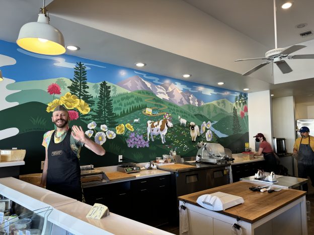 Andrew standing behind the cheese counter in front of our mural.